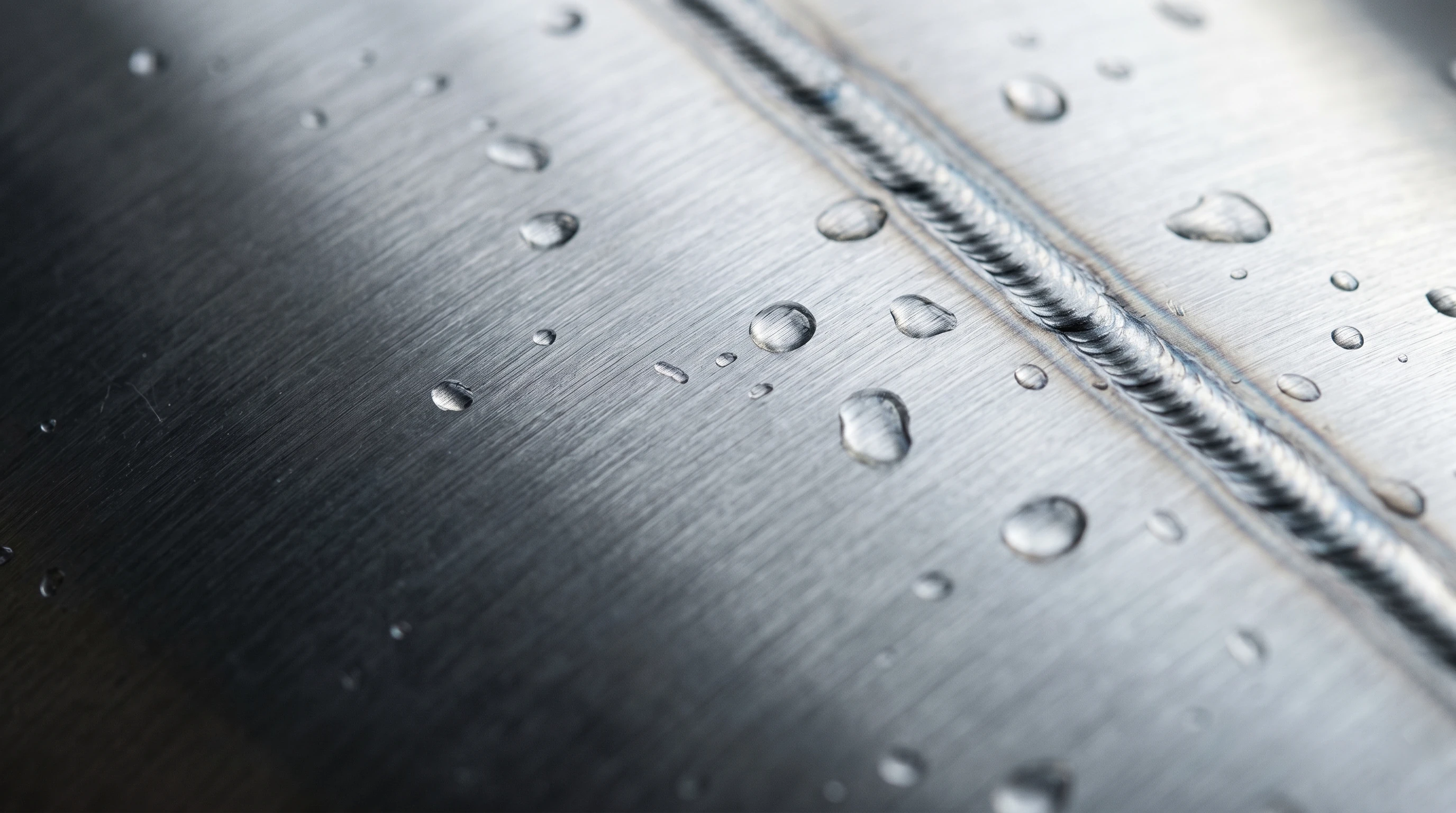 Water droplets on a brushed stainless steel surface with a weld seam