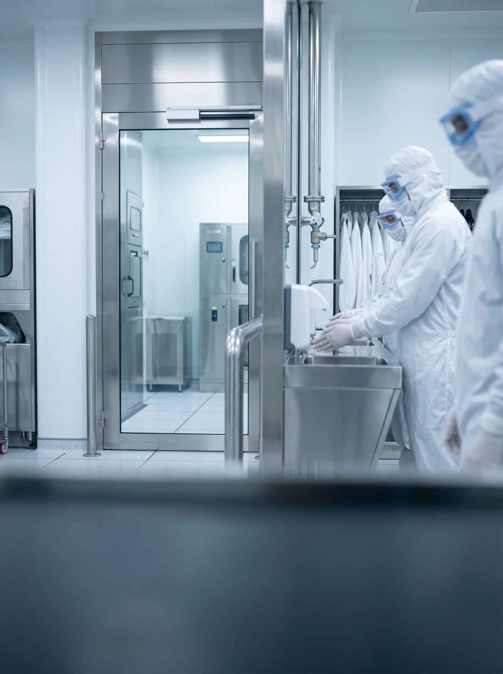 Staff in protective clothing washing their hands at a glass-partitioned cleanroom entrance